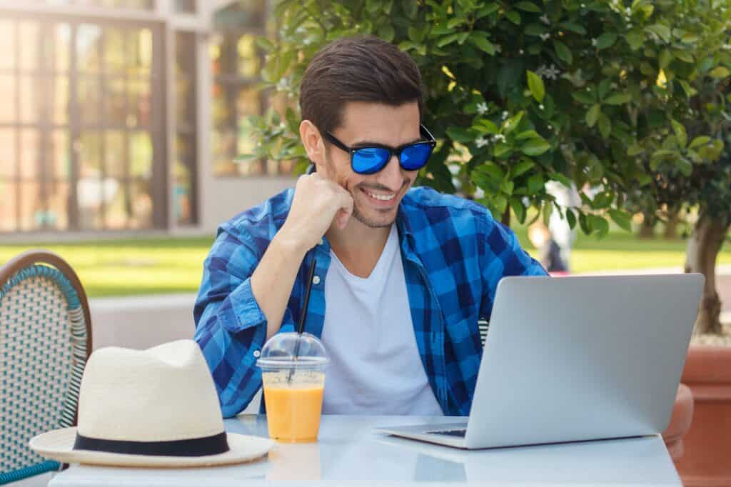 Attractive smiling handsome man sitting in cafe, spending leisure time, working on laptop