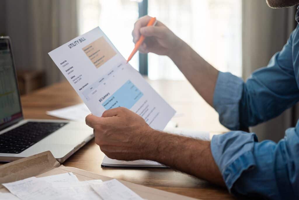 Businessman with pen checks utility bill debt sitting at desk with laptop payments regulation